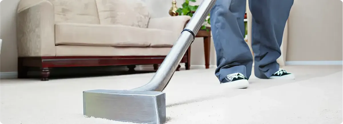 Carpet cleaning technician using a hot-water extraction wand on a light-colored carpet in a living room, Oakland, CA.